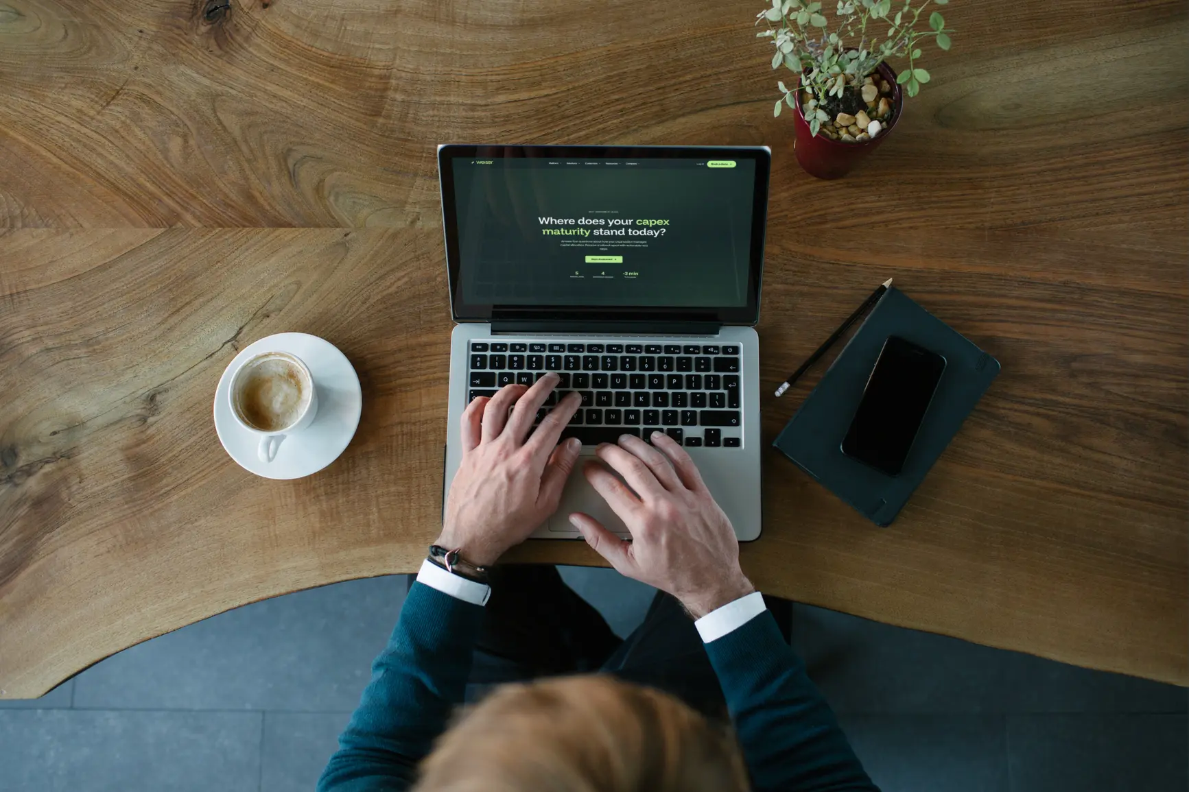 Top-down view of a person at a wooden desk with the Weissr Capex Maturity Assessment open on their laptop